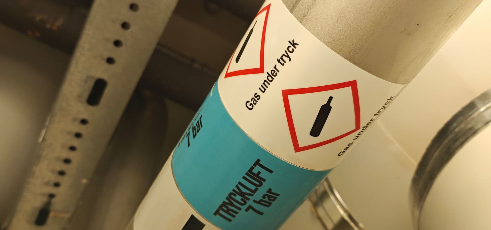 Bilden visar rörmärkning med tydlig indikering på innehåll, flödesriktning och faropiktorgam.